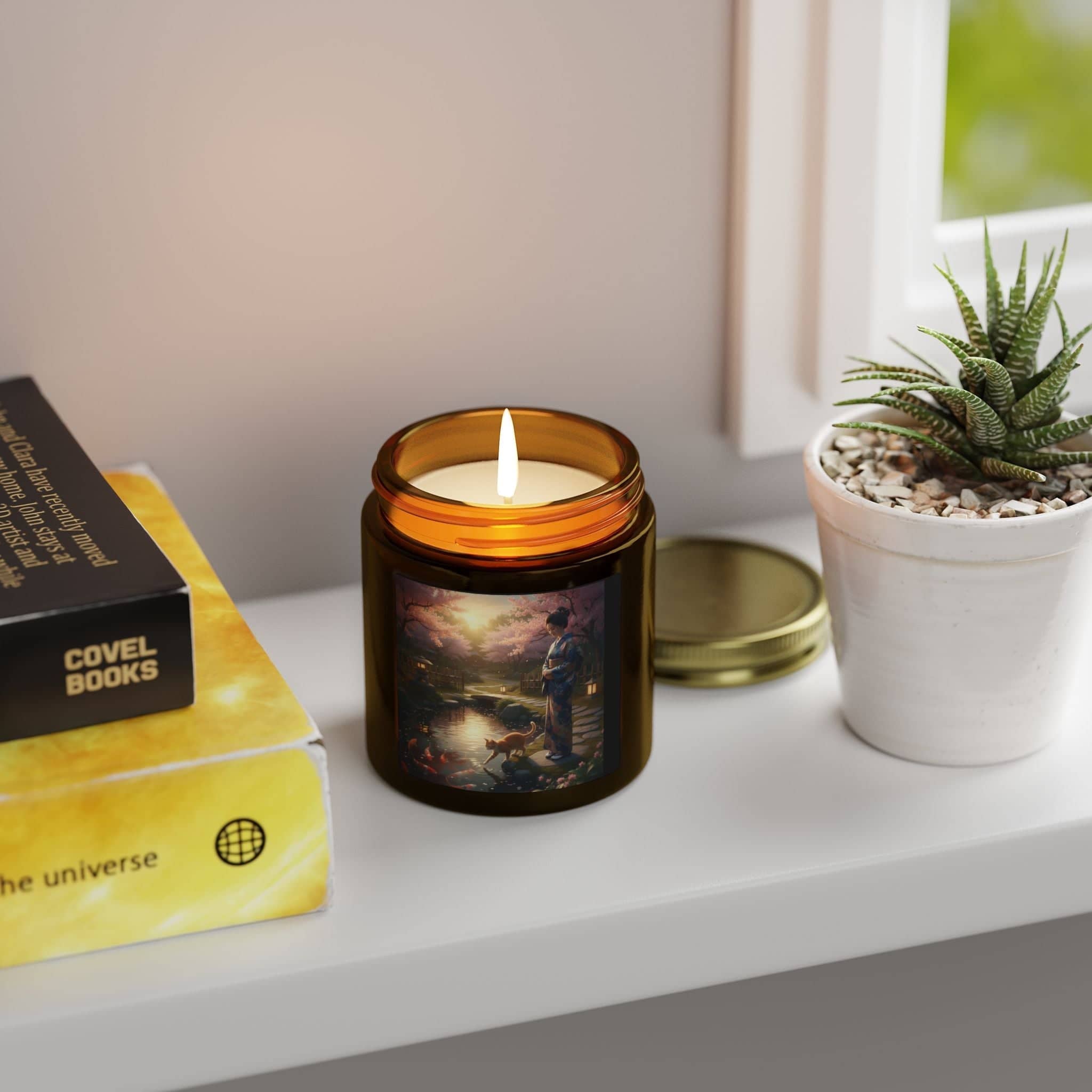 Artistic candles for home decor in amber glass jar with painted label on white windowsill next to books and potted plant