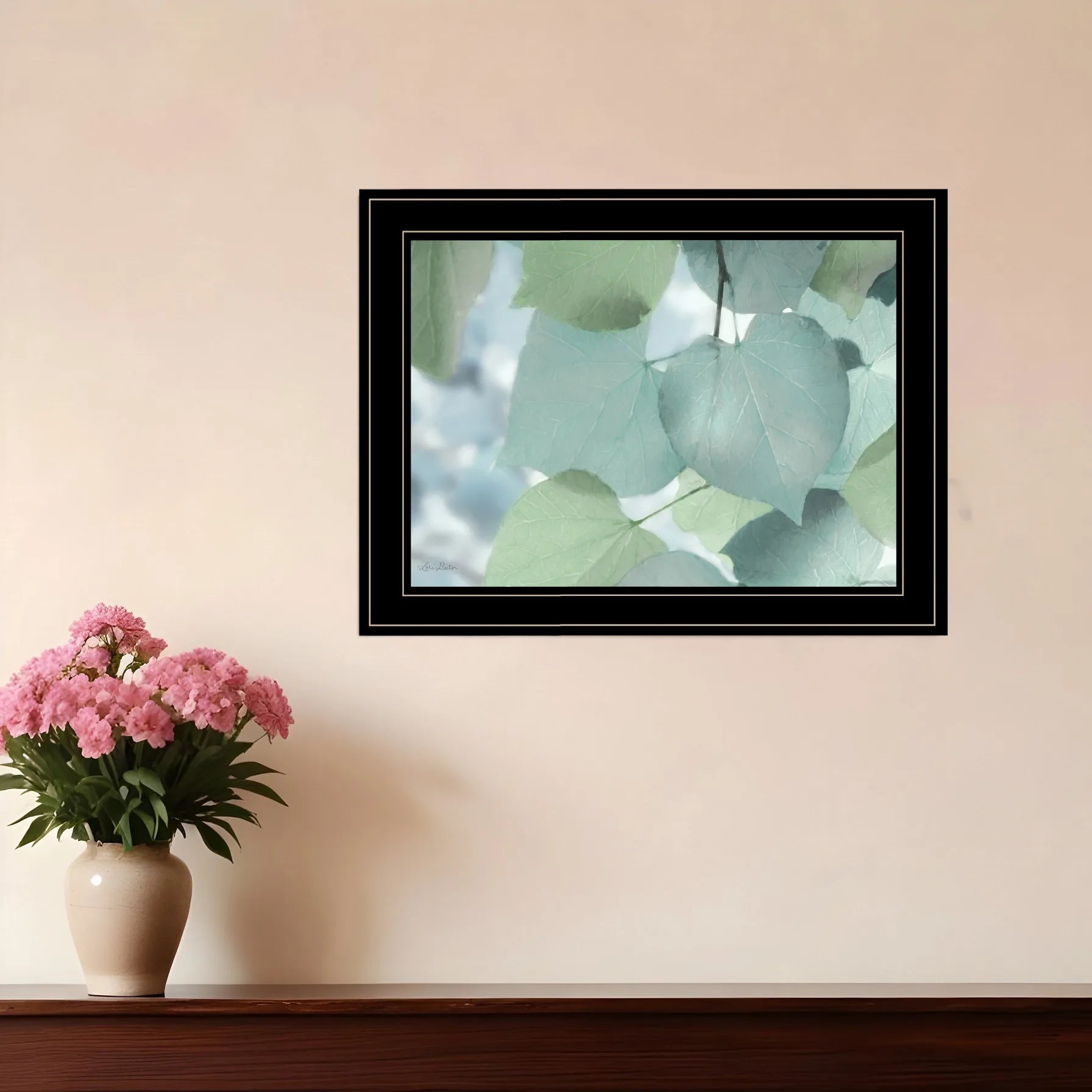 Framed AI generated leaf wall art with soft green leaves hanging on a beige wall above wooden shelf with pink flowers